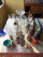 Table display of assorted glassware, metal shakers, ice bucket, bowl and wood-stand cups