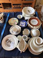 Full assortment of assorted china on dark blanket showing many plates, bowls, and cups