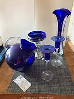 Five cobalt blue glass items and one silver and glass centerpiece bowl arranged on a table.