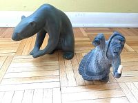 Both stone sculptures shown together: black bear in crouching stance and detailed hunter figure in traditional clothing.