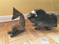 Both bull and mermaid stone sculptures displayed side by side on hardwood floor against yellow wall
