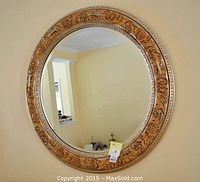 Front view of the large circular wall mirror showing the natural wood frame with intricate floral carvings accented in silver and black.