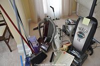 Photo shows multiple vacuum cleaners including World Vac Featherweight upright, Hoover canister, Oreck XL upright, Black and Decker DustBuster handheld, alongside broom, dustpan, and Swiffer WetJet.