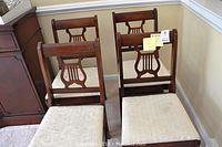 Four wooden chairs with lyre backs and cream upholstered seats arranged together showing overall color and style.