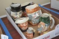 Seven ceramic character mugs in white cardboard box showing various facial designs and hats.