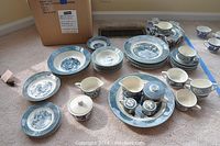 Wide shot displaying the china set arranged on carpet including plates, bowls, teacups, platters, and shakers