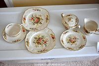 Top view of a selection of Marlborough Royal Petal china pieces including a teacup, saucer, two plates, creamer, and sugar bowl showing floral patterns and gold trim.