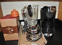 Photo showing ceramic hot chocolate pot in box, Osterizer blender with glass jar, and Black and Decker coffee maker without pot on kitchen counter.