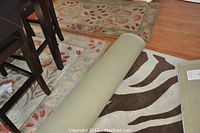 Dining area scene with two unrolled floral rugs and a rolled zebra-print rug under table and chairs