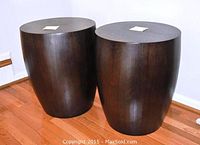 Two barrel-shaped side tables upright on hardwood floor against white wall.