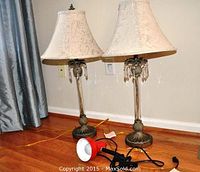 Two ornate table lamps with cream-colored floral fabric shades and brass-tone bases, plus one small red desk lamp on hardwood floor.