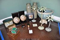 Overview of decorative pottery vases, large bowl, palm tree candle holders, globe bookends, and wooden boxes on a countertop.