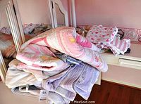 Stack of folded pink and purple quilts, some pillow shams visible