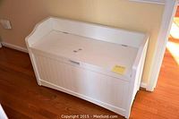 White wooden storage bench, front and side view showcasing paneled design and overall shape.