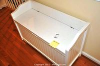 White wooden bench with panel design, closed lid showing curved sides and smooth top surface.