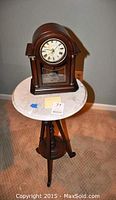 Mini grandfather clock placed on a round marble top wooden side table/plant stand, showing overall arrangement.