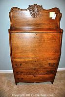 Front view of closed drop-front desk showing carved crest and lower drawers