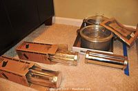 Two metal pots with glass lids along with several stainless steel Pampered Chef bread tubes in original packaging placed on floor carpet.