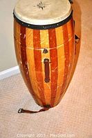Full side view of the large wooden drum showing striped wood pattern and leather strap attached near the base.