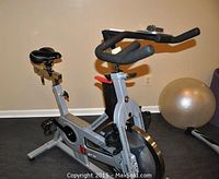 Side overview showing frame, seat, handlebars, flywheel and pedals