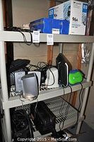 Full view of plastic shelf unit containing all items in lot, including HP toner cartridge boxes, silver speakers, computer keyboard, monitor, and a green/blue radio.