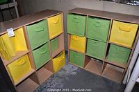 Two wooden cubby units with nine compartments each, some with green and yellow cloth baskets inside, placed on concrete floor.