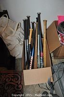 Box full of assorted baseball and softball bats with metal and wooden handles, some showing signs of wear