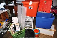 Photo showing organizational bins including a large orange Sterilite 18-gallon bin, blue and green bins, a white organizing drawer unit, and other storage items.