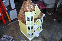 Front-left angled view of the yellow wooden Victorian style dollhouse with turret and shingled roof