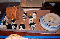 Photo showing nine mini Dutch ceramic houses in white with black roofs and yellow chimneys along with a woven basket tray and covered pottery dish with lid.