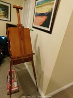 Full front view of assembled tripod easel leaning against wall with lamp box at base