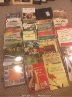 Photo shows an extensive variety of paint instruction books arranged on carpet, including titles on landscapes, animals, watercolor, pen & ink, acrylic, and color art.