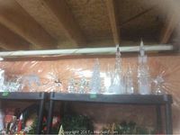 Wide view of clear plastic Christmas trees, reindeer, and other decorations on black shelving against a wood panel wall.