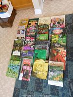 Collection of over 25 gardening books arranged on carpet and floor, visible variety of topics and vibrant covers.