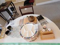Table with five Villeroy and Boch fondue plates, clear glass ramekins, ceramic knife rests, wooden salt/pepper and napkin holder with chef shakers, cheese cutting board, fondue pot and knives.