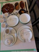 Photo showing Corelle dinnerware pieces including cups with saucers, plates, bowls, sugar bowl, creamer, and hand-carved wooden bowls on a table