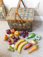 Picnic basket and assortment of life size wood fruit and vegetables arranged on carpet floor.