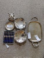 Full view of all vintage silverplated items laid out on carpet including trays, bowls, lobster forks in case, and wine bottle warmer.