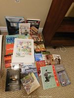 Overview photo showing multiple books stacked on carpet with different topics like Tai Chi, home restoration, cottage water systems, medical, and inspirational books.