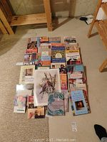 Photo showing a collection of over 30 craft and art books spread on the floor with topics including sewing, quilting, paint effects, stenciling, stamp designs, and crafts techniques.