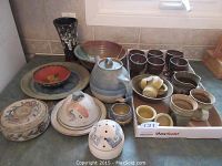 General view of assorted pottery including cups, bowls, covered dish and plates on kitchen counter.