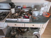 View of countertop and open cabinet showing lidded pots, glass measuring cups, cooking utensils, two metal loaf pans, and a small slow cooker.