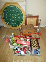 Wide shot showing the large octagonal marble game board propped against the wall with the labyrinth ball maze game, crokinole board, chess board, boxed Mille Bornes card game and assorted buttons and patches on the floor. Also visible AM/FM headset.