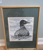 Framed print of a loon bird on water in black and white with light wooden frame.