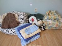 Curtains, towels, comforter, sheep-themed flower pot, brown knit hat, and embroidered floral decoration arranged on floor