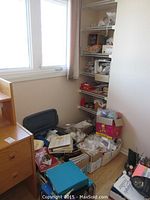 Corner of a room with multiple boxes, plastic bins, and containers filled with yarn, fabric, and various craft supplies piled on the floor and on shelving.