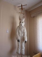Full view of puppet hanging from ceiling showing white fur body and wooden control