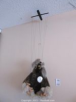 View of entire marionette puppet hanging with strings, showing fur body, hands, and facial features.