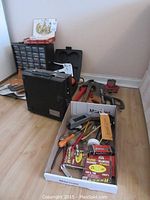 Overview photo showing the drill case, tool box with hand tools, red pipe wrench, and vise, plus other items spread on floor
