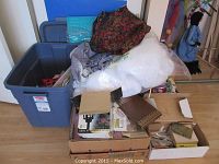 Overview of large blue storage bin filled with fabric, quilt batting, and other crafts materials alongside cardboard boxes containing stamps and supplies.